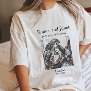 May include: A white t-shirt with a black print of a vintage book cover featuring an illustration of Romeo and Juliet. The text on the shirt reads "Romeo and Juliet" by William Shakespeare, "London 1591-1596".