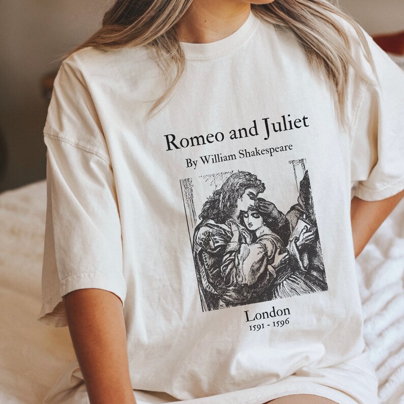 May include: A white t-shirt with a black print of a vintage book cover featuring an illustration of Romeo and Juliet. The text on the shirt reads "Romeo and Juliet" by William Shakespeare, "London 1591-1596".