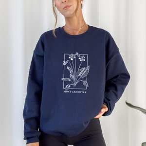 May include: A navy blue sweatshirt with a white floral graphic and the text "MOST ARDENTLY" printed on the front.