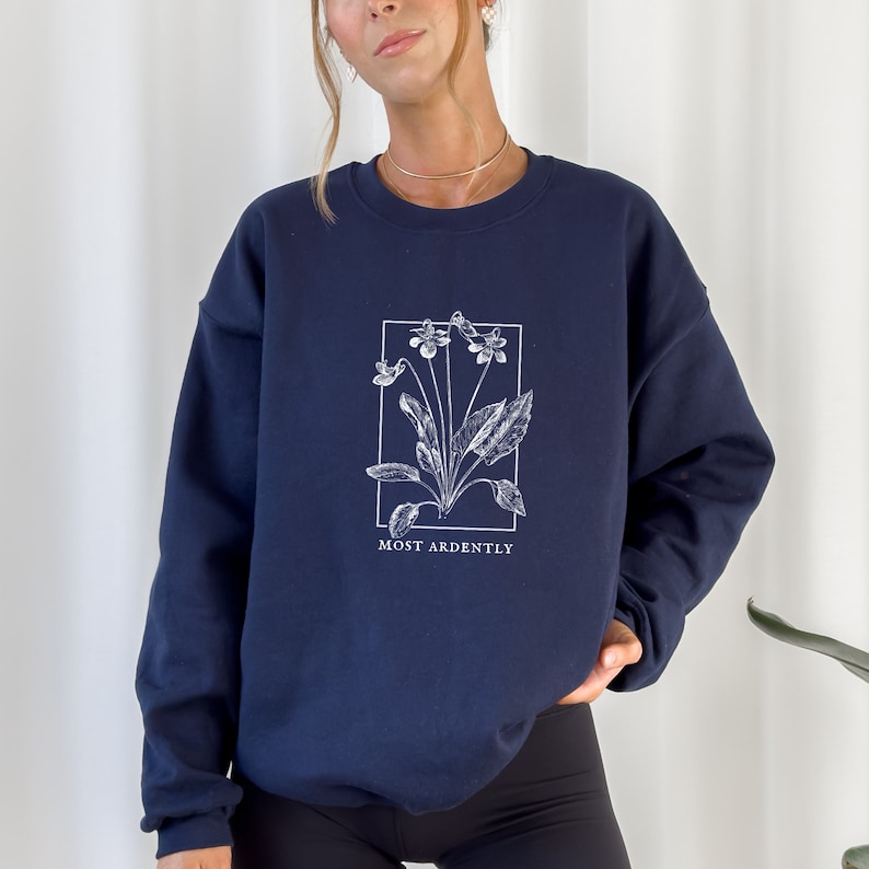 May include: A navy blue sweatshirt with a white floral graphic and the text "MOST ARDENTLY" printed on the front.
