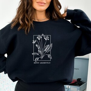 May include: Black sweatshirt with a white floral graphic and the text "MOST ARDENTLY" printed below the graphic.