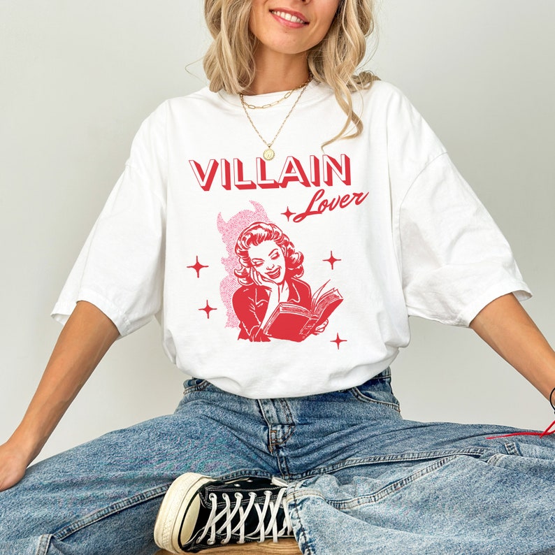 May include: White t-shirt with a red graphic of a woman reading a book with the text "VILLAIN Lover" above her.