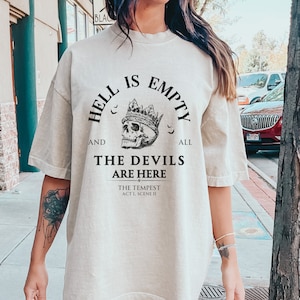 May include: A beige t-shirt with a black graphic print that reads "Hell is empty and all the devils are here. The Tempest Act 1, Scene II". The graphic also includes a skull wearing a crown.