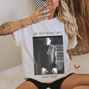 May include: White t-shirt with a black and white image of a man with a caption that reads "You must bounce on it Crazy Style."