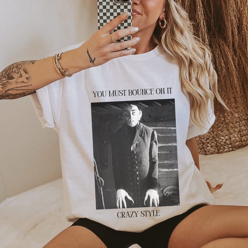 May include: White t-shirt with a black and white image of a man with a caption that reads "You must bounce on it Crazy Style."