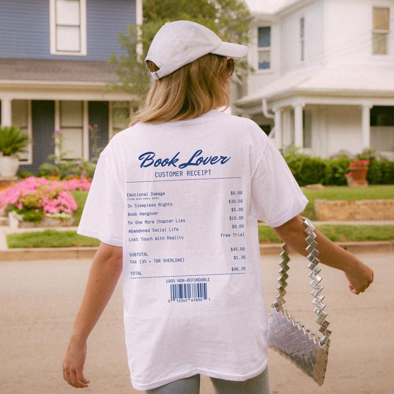 May include: White t-shirt with the text "Book Lover" and a customer receipt design printed on the back. The receipt lists fictional items like "Emotional Damage" and "Book Hangover". The shirt also has a barcode.