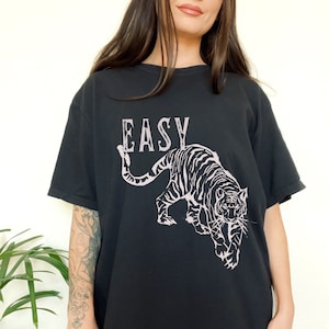 May include: Black t-shirt featuring a pink tiger graphic and the word "EASY" printed on the front.