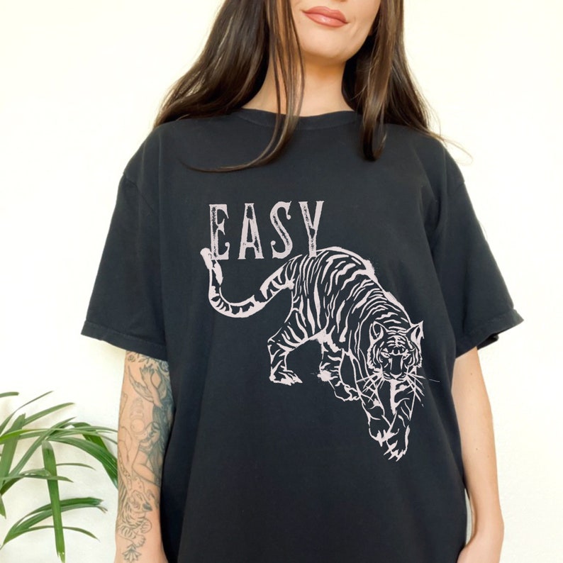 May include: Black t-shirt featuring a pink tiger graphic and the word "EASY" printed on the front.