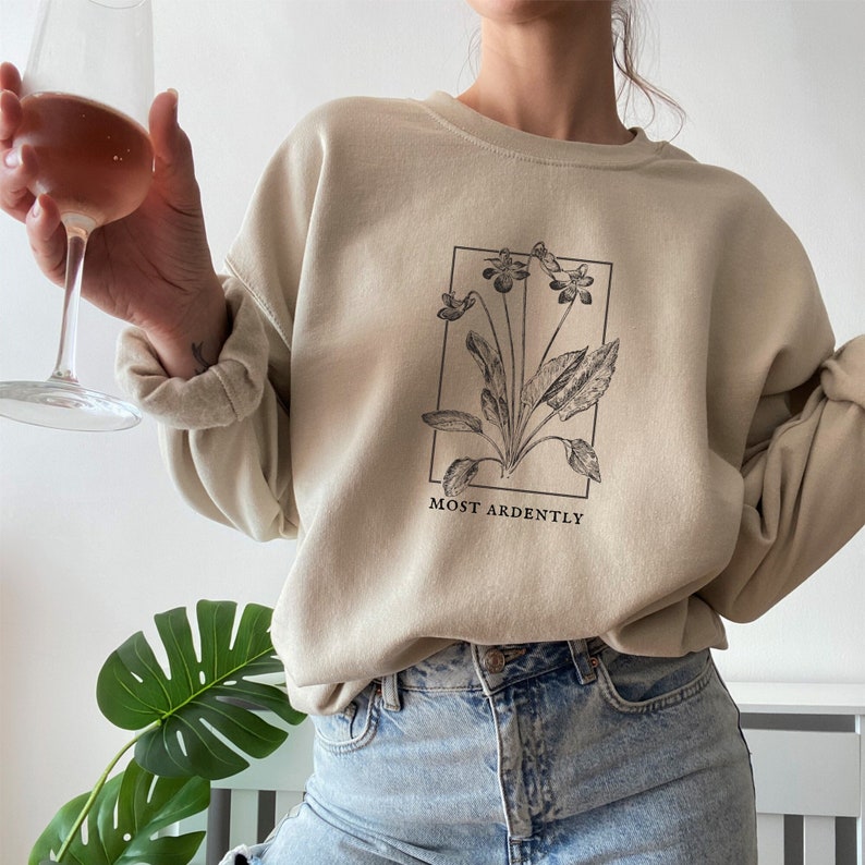 May include: A beige sweatshirt with a black floral graphic and the text "MOST ARDENTLY" printed on the front.