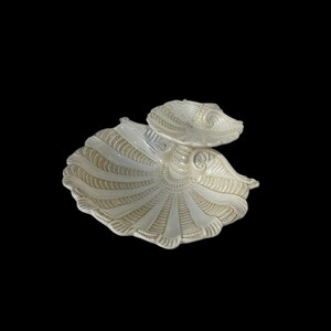 May include: A white ceramic serving dish shaped like a seashell. The dish is divided into two sections, one larger than the other. The dish has a textured surface and a glossy finish.