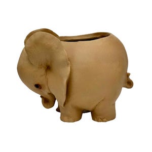 May include: A light brown ceramic elephant planter with a large opening for planting. The planter is shaped like an elephant with its trunk curled down and its ears perked up.