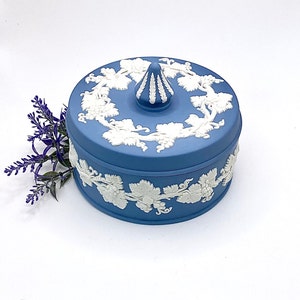 May include: A blue ceramic trinket box with a white grape vine design. The box has a round shape with a lid and a decorative finial. The grape vine design is repeated around the box.