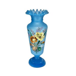 May include: A blue glass vase with a ruffled rim and a flared base. The vase is decorated with hand-painted flowers in shades of yellow, orange, and white, with green leaves and stems. The vase is approximately 10 inches tall.
