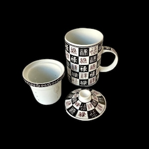 May include: White ceramic teacup with a black and white design featuring Chinese characters. The teacup has a built-in strainer and a matching lid.