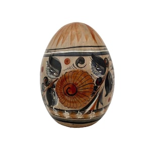 May include: A decorative, hand-painted ceramic egg. The egg features a tan base with a floral design in shades of brown, black, and white. The top of the egg has a textured, carved pattern. The egg is a unique piece of home decor.