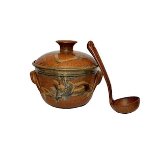 May include: A brown and black ceramic soup tureen with a lid and a matching ladle. The tureen has a unique glaze pattern with brown, orange, and black swirls.