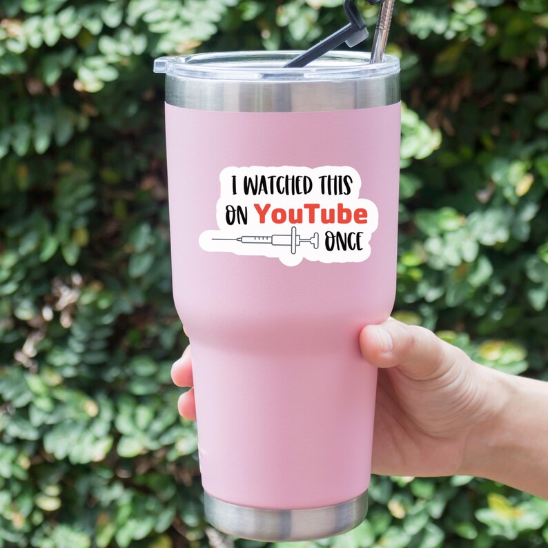 Puede incluir: Un vaso t&eacute;rmico rosa claro con borde plateado y pajita negra. El vaso tiene una pegatina blanca con el texto "I WATCHED THIS ON YouTube ONCE" y un gr&aacute;fico de jeringa.