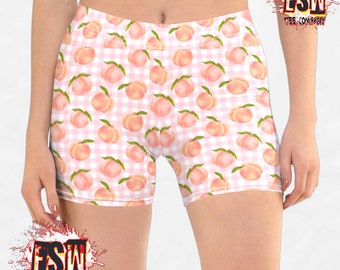 Op de afbeelding: Roze en witte gingham print sport shorts met een perzik patroon. De shorts zijn gemaakt van een rekbare, comfortabele stof en perfect voor het sporten of boodschappen doen.