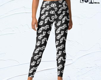 Puede incluir: Leggings negros con un estampado floral blanco. Los leggings de cintura alta presentan un diseño repetido de flores blancas sobre un fondo negro. Los leggings son ajustados y adecuados para diversas actividades.