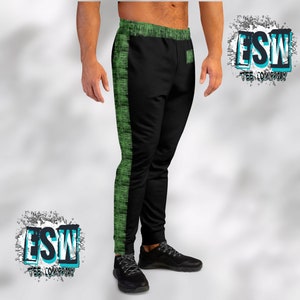 Pode incluir: Calça de moletom preta com painéis laterais verdes e um pequeno bolso na perna direita. A calça de moletom tem cós com cordão e um logotipo na lateral que diz "ESW Tee Company".