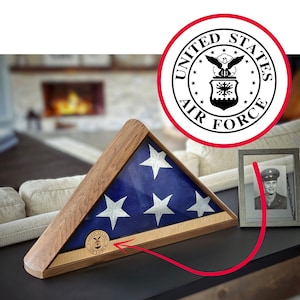 Könnte beinhalten: Holz-Fahnenvitrine mit einer gefalteten amerikanischen Flagge im Inneren. Die Flagge ist blau mit weißen Sternen und einem weißen Streifen. Die Vitrine hat einen Holzrahmen und ein Emblem der US Air Force.