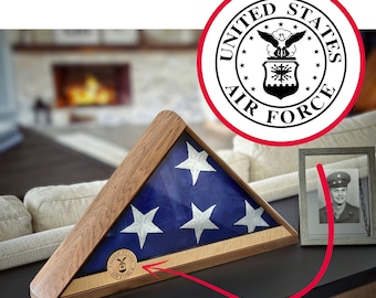 May include: Wooden flag display case with a folded American flag inside. The flag is blue with white stars and a white stripe. The case has a wooden frame and a United States Air Force emblem.