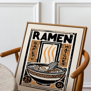 Pode incluir: Um cartaz de estilo vintage com a palavra "RAMEN" em letras pretas em negrito. O cartaz apresenta uma tigela de macarr&atilde;o ramen com ovos, carne e vegetais. A tigela &eacute; cercada por uma borda preta e branca com um padr&atilde;o repetitivo. O cartaz est&aacute; sobre um fundo bege claro e tem uma moldura de madeira marrom.