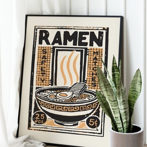 Pode incluir: Um p&ocirc;ster emoldurado em preto com um design vintage que apresenta uma tigela de macarr&atilde;o ramen com o texto "RAMEN" em letras pretas em negrito. O p&ocirc;ster tem um esquema de cores amarelo e laranja com acentos pretos.