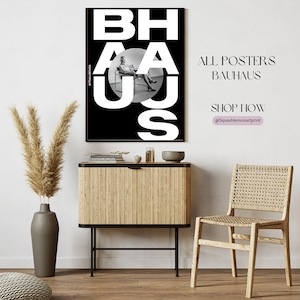 May include: A black and white poster with the word "BAHAUS" in large white letters. The poster features a black and white photo of a person sitting in a chair. The poster is hanging on a white wall above a wooden cabinet and a woven chair.