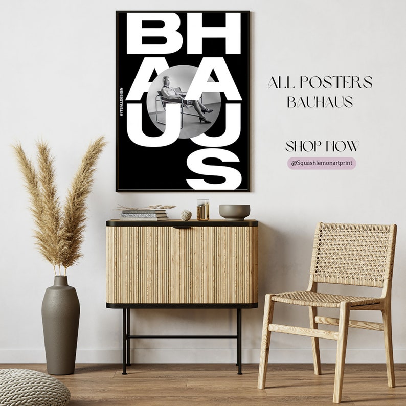 May include: A black and white poster with the word "BAHAUS" in large white letters. The poster features a black and white photo of a person sitting in a chair. The poster is hanging on a white wall above a wooden cabinet and a woven chair.