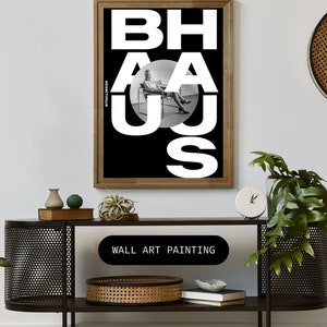 May include: Black and white wall art painting with the word "BAHAUS" in large white letters. The letters are overlapping and a person is sitting in a chair in the middle of the word.