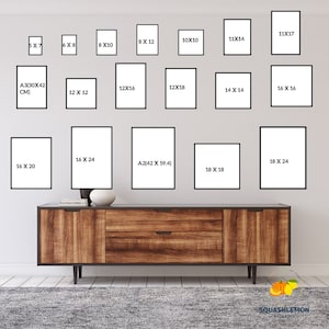 May include: A white wall with a variety of black picture frames of different sizes. The frames are arranged in a grid pattern. The frames are all empty. A wooden dresser is in front of the frames. The dresser has two drawers and a brown top. The dresser is sitting on a gray rug.