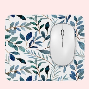 May include: A white computer mouse rests on a rectangular mousepad. The mousepad features a watercolor pattern of blue and green leaves on a white background. The mouse is a simple, modern design.