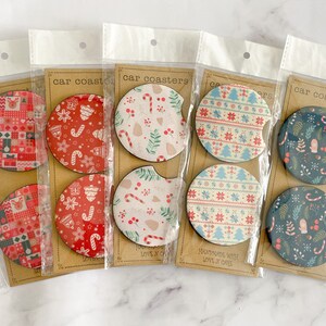 May include: Four sets of Christmas-themed car coasters. Each set includes two coasters with different designs. The coasters are made of wood and have a variety of patterns, including snowflakes, candy canes, and Christmas trees. The text on the packaging reads "Handmade Wood Love & Care".