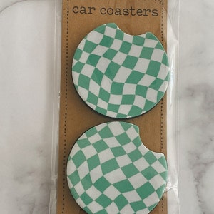 Pu&ograve; includere: Due sottobicchieri per auto a scacchi verdi e bianchi in una confezione di plastica. La confezione ha uno sfondo marrone con il testo "car coasters" stampato su di essa.