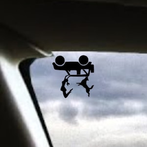 Op de afbeelding: Zwarte silhouet van een omgekeerde auto met twee mensen die er vandoor gaan. De auto staat op een witte achtergrond.