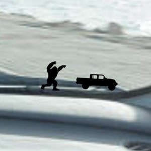 May include: A black silhouette of a Bigfoot running towards a black pickup truck. The image is a sticker for a car window.