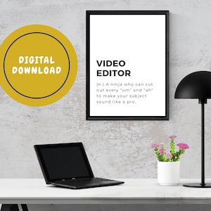 Könnte beinhalten: Ein gerahmter schwarzer Druck mit dem Text "VIDEO EDITOR" und einer Definition. Ein schwarzer Laptop, eine schwarze Schreibtischlampe und ein kleiner weißer Topf mit rosa Blumen stehen auf einem weißen Schreibtisch. Ein gelber Kreis mit "DIGITALER DOWNLOAD" befindet sich oben links.