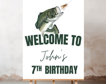 May include: Welcome to John's 7th Birthday sign with a green bass fish jumping out of the water and a green fly on a fishing line. The sign is white with green text.