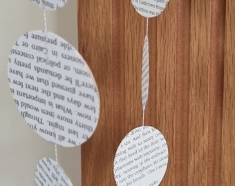 May include: A garland of white paper circles with black text from a book hanging against a wood background. The text on the circles is from a novel.