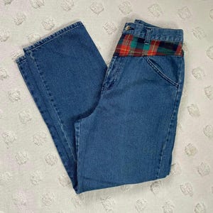 May include: Blue denim jeans with a plaid waistband. The plaid is red, green and black.