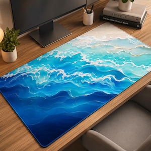 Puede incluir: Una alfombrilla de escritorio rectangular con un diseño de olas oceánicas en degradados de azul marino profundo, turquesa brillante y espuma de mar blanca. La superficie muestra un patrón fluido y superpuesto de olas rompiendo hacia la arena clara.
