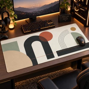 May include: A rectangular desk mat featuring an off-white base with geometric shapes including a large black arch, a terracotta circle, a sage green rectangle, and a tan semi-circle. Thin black lines form an arc pattern above a horizontal line.