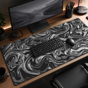 May include: A rectangular desk mat featuring a monochromatic marbled pattern in shades of black, white, and gray. The surface displays fluid, swirling abstract shapes across the entire area, providing a base for a black computer keyboard and mouse.