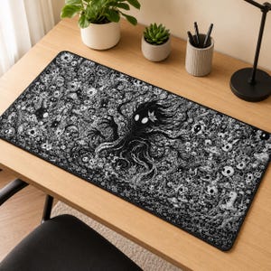 May include: A rectangular desk mat featuring a detailed black and white illustration of a central shadowy figure with glowing white eyes, surrounded by a dense forest scene filled with small creatures, mushrooms, and intricate floral patterns.