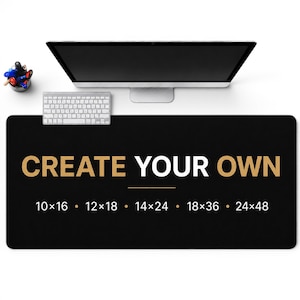 May include: A large black rectangular desk mat featuring the gold and white text "CREATE YOUR OWN" followed by a list of available dimensions in inches: 10x16, 12x18, 14x24, 18x36, and 24x48, positioned below a computer monitor and a white keyboard.