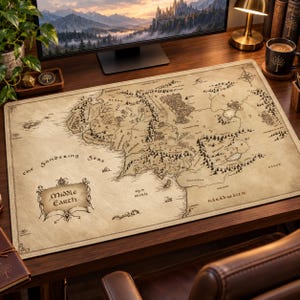 May include: A rectangular desk mat featuring a detailed, vintage-style map of Middle-earth. The beige surface displays intricate black line drawings of mountains, forests, and coastlines, with the text Middle Earth in a decorative frame.