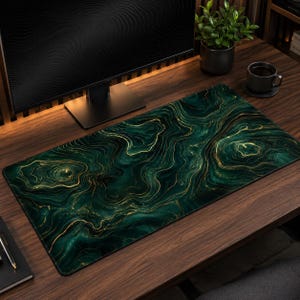 Puede incluir: Una alfombrilla de escritorio rectangular con un patrón de mármol en verde esmeralda oscuro y negro con vetas doradas fluidas. La superficie tiene una textura suave y cubre una parte importante del escritorio de madera, ofreciendo un área amplia para periféricos.