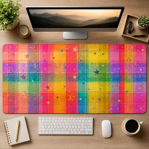 Puede incluir: Una alfombrilla de escritorio rectangular con un vibrante patrón de cuadros multicolor en tonos rosa, naranja, amarillo, verde y azul. La superficie está decorada con numerosas estrellas pequeñas dispersas en varios colores y acabados metálicos.