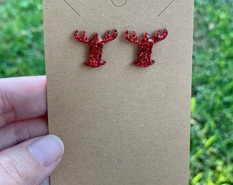 May include: A pair of red glitter lobster earrings. The earrings are on a brown card.